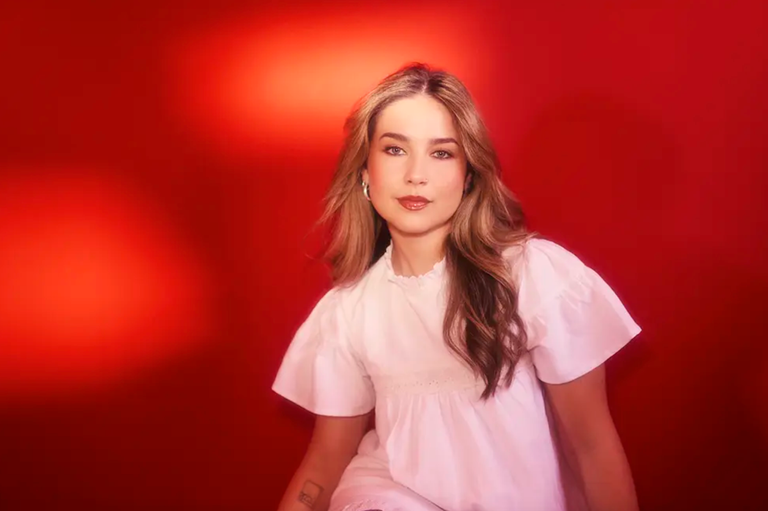 Studio portrait of Australian musician Jem Cassar-Daley wearing a white ruffled top against a bold red background.